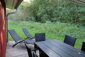 Eine Terrasse im Freien mit einem Holztisch und vier Stühlen, umgeben von viel Grün.