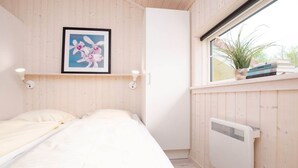 Ein Schlafzimmer mit einem Bett, einem gerahmten Bild an der Wand, einem Heizkörper und einem Fenster mit Pflanze und Büchern auf der Fensterbank.