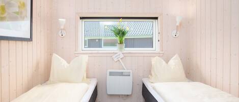 A room with two beds, a window with a plant, and a small heater.