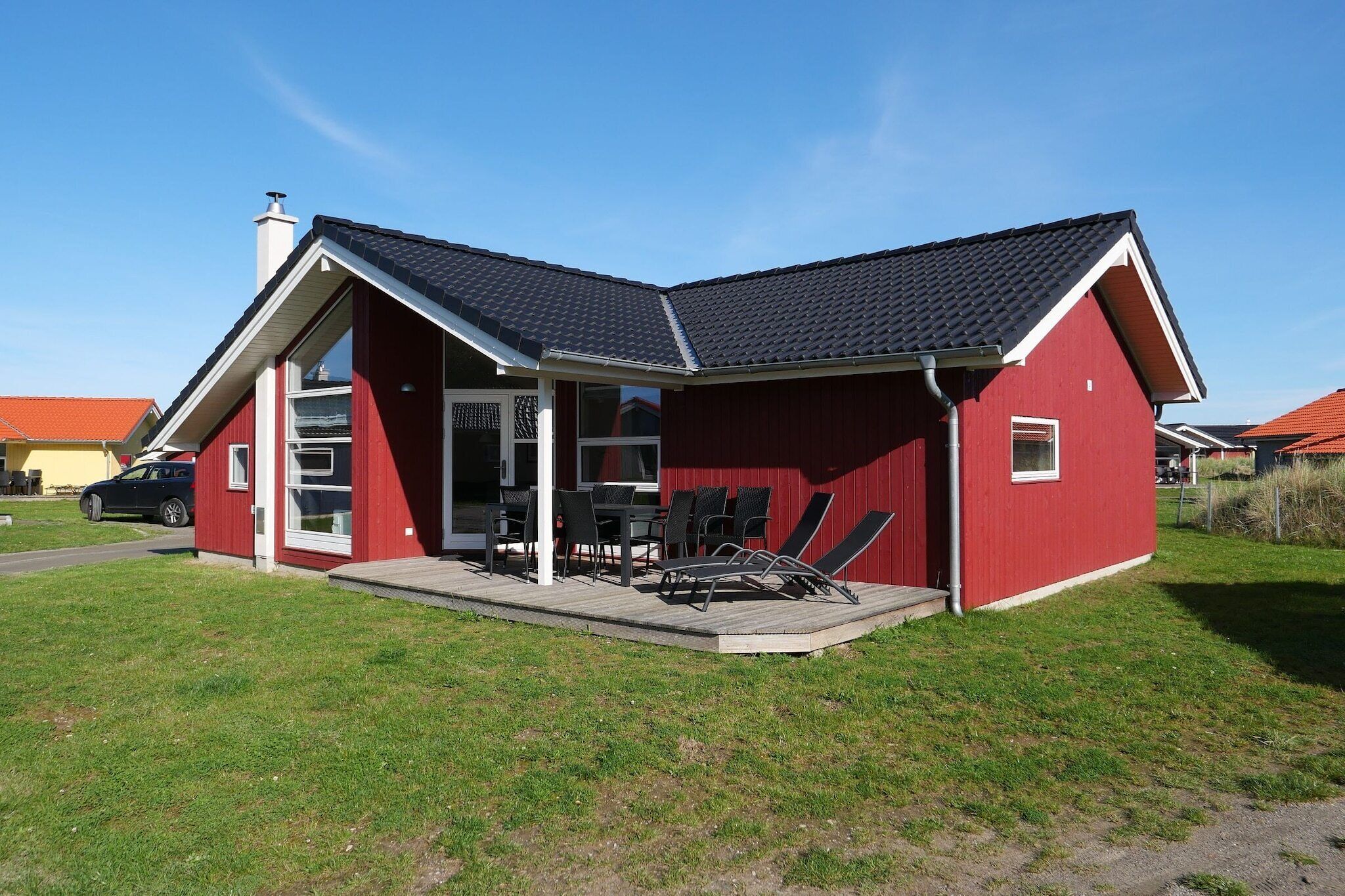 A red building with a sloped roof, a covered porch with outdoor furniture, and a car parked in front.