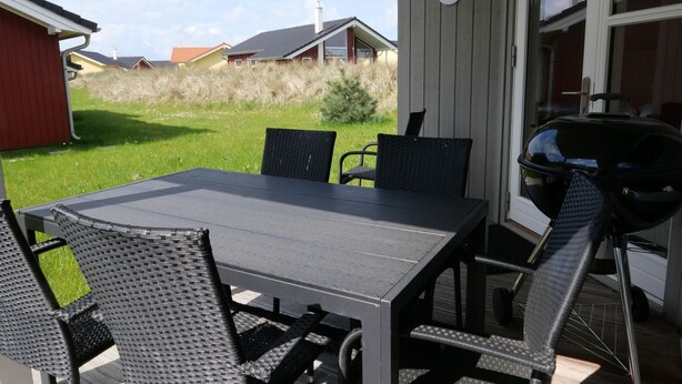 An outdoor patio with a table and chairs, a barbecue grill, and a house number 114 in the background. - Grobenbrode Küstenurlaub (Großenbrode)