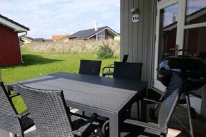 Une terrasse extérieure avec une table et des chaises, un barbecue et, au fond, le numéro de la maison, qui est le 114.