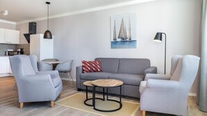 A modern living room with a grey sofa, two armchairs, a coffee table, and a painting of sailboats on the wall. - Apartment in Strand- und Parknähe (Travemünde)