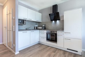 Una cocina moderna con armarios blancos, microondas, cafetera y estufa.