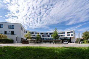 A modern multi-story building with a flat roof, large windows, and a covered entrance area. - Apartment in Strand- und Parknähe (Travemünde)
