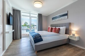 A modern hotel room with a large bed, a flat-screen TV, a balcony with a view, and a painting on the wall. - Apartment in Strand- und Parknähe (Travemünde)