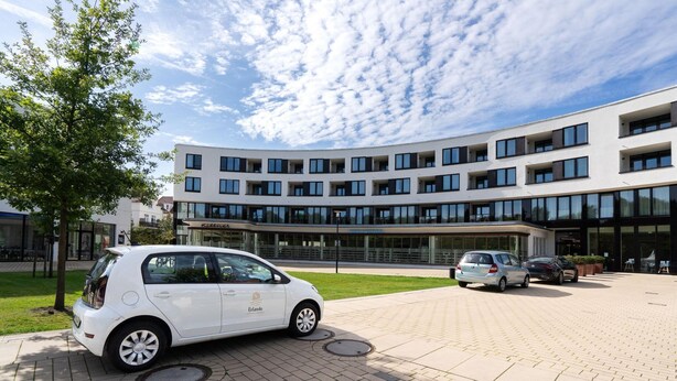 A modern building with a flat roof, large windows, and a paved entrance area with cars parked. - Apartment in Strand- und Parknähe (Travemünde)