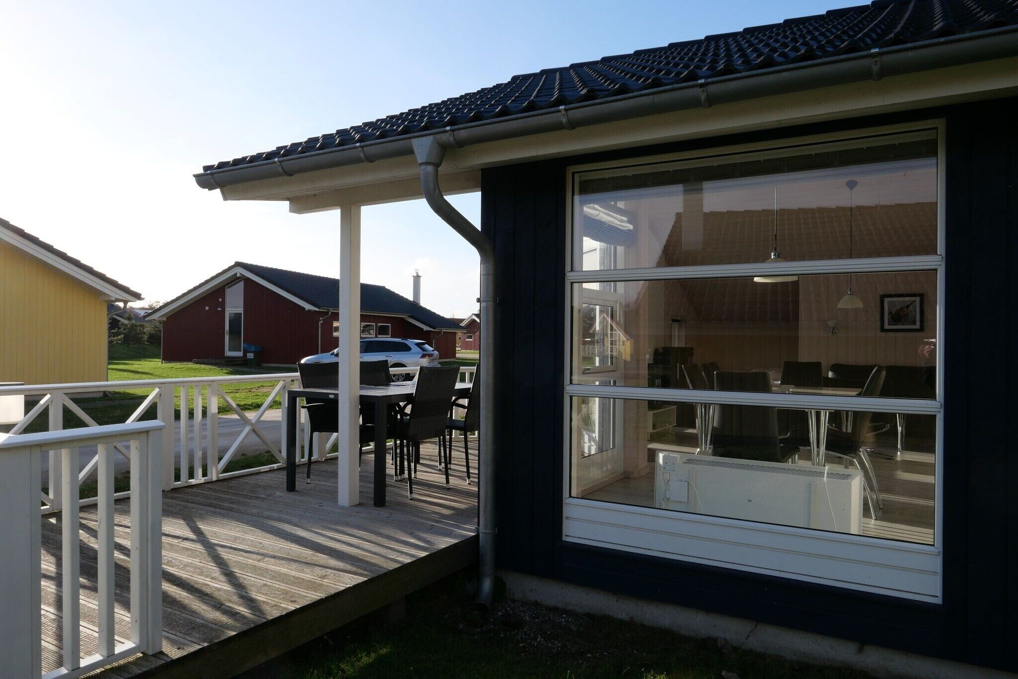 A residential building with a covered porch, a dining area with chairs and a table, and a view of the backyard.