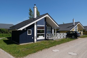 A small, single-story building with a dark exterior, a white porch railing, and a chimney. - Übernachten Sie in der Nähe des Dünenspielplatzes. (Großenbrode)