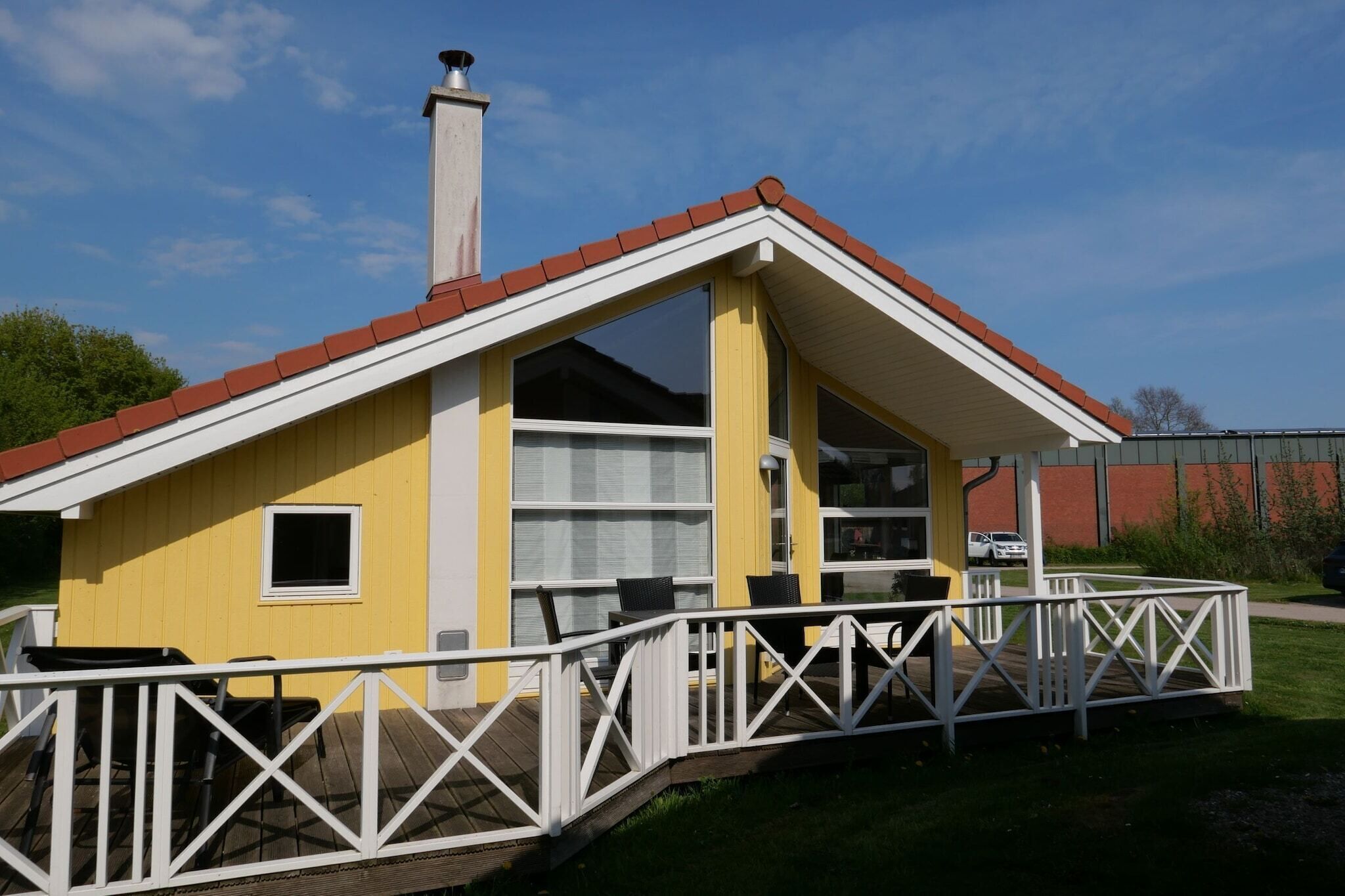 Un edificio amarillo con techo blanco y una chimenea, que cuenta con una zona de estar exterior cubierta y una barandilla blanca.