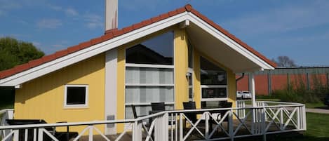 Un edificio amarillo con techo blanco y una chimenea, que cuenta con una zona de estar exterior cubierta y una barandilla blanca.