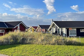 A row of houses with pitched roofs and large windows, surrounded by grassy fields. - Hübsches Familienhaus mit Spa (Großenbrode)
