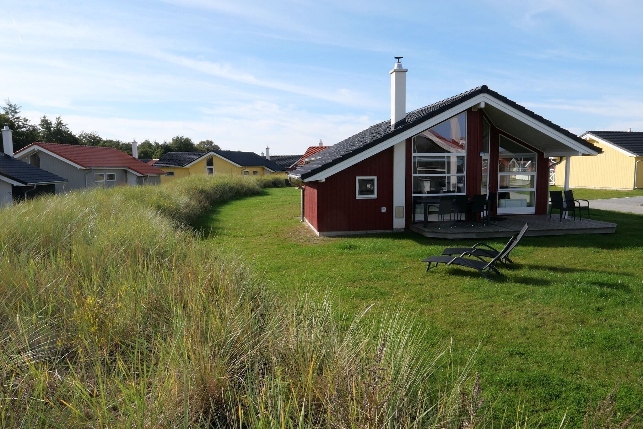 A red building with a sloped roof and a chimney, surrounded by grass and other houses.