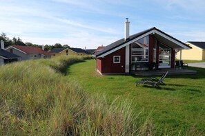 Ein rotes Gebäude mit geneigtem Dach und Schornstein, umgeben von Gras und weiteren Häusern.