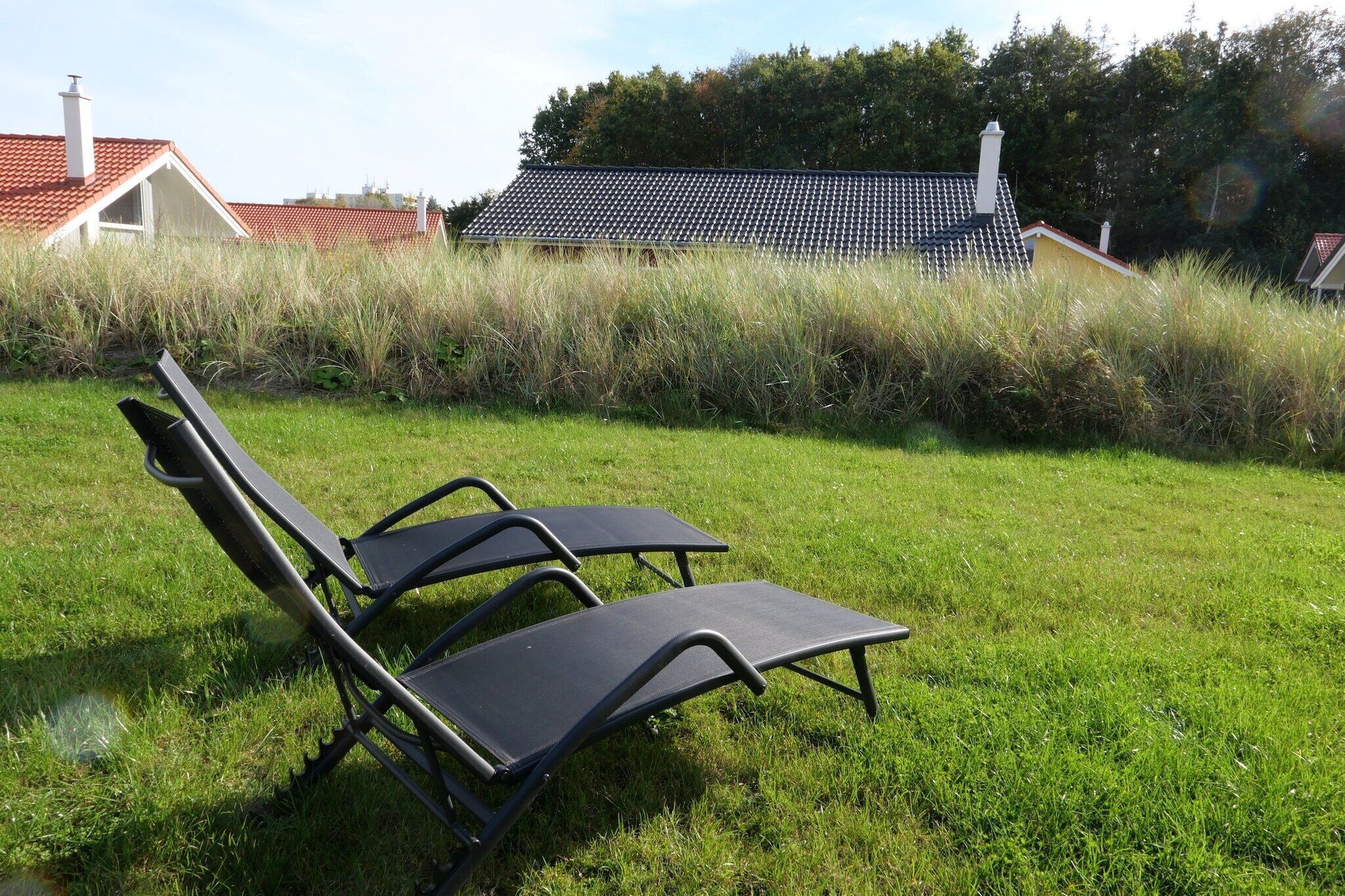 Dos sillones de exterior en un césped, con una casa al fondo.