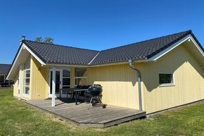 Ein eingeschossiges Haus mit einer überdachten Terrasse, einem Grill und einem Fenster.