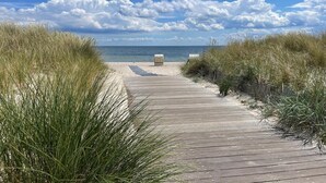 Een houten looppad dat naar een strand leidt, met zandduinen aan weerszijden.