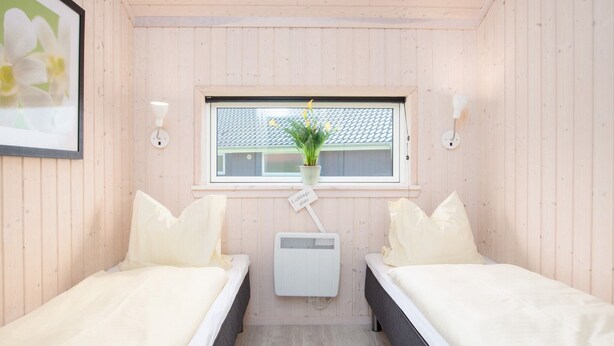 Een kamer met twee bedden, een raam met een plant en een kleine verwarming.