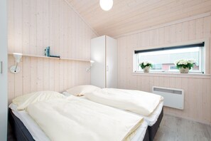 Un dormitorio con dos camas, una ventana con plantas en macetas, un radiador y una estantería con libros.
