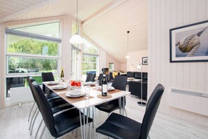 A dining area with a table set for four, black chairs, and a view of the outdoors through large windows. - Spa-Haus in der Nähe von South Beach (Großenbrode)