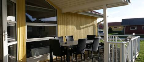A covered patio with a table and chairs, a wooden deck, and a white railing.