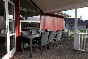 Eine überdachte Terrasse im Freien mit einem Esstisch und Stühlen, einer Schiebeglastür und Blick auf eine Wohngegend.