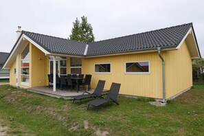 A yellow building with a covered patio, a table with chairs, and a lawn. - Grobenbrode Escape für 10 (Großenbrode)