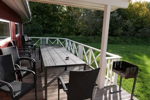 A covered outdoor patio with a table and chairs, a grill, and a white railing. - Großes Familienhaus mit Spa (Großenbrode)