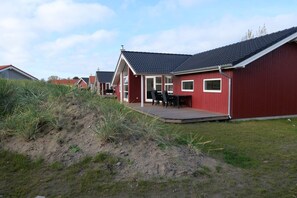 Une rangée de maisons rouges aux toits sombres, une zone herbeuse avec de l’herbe haute et un ciel dégagé.