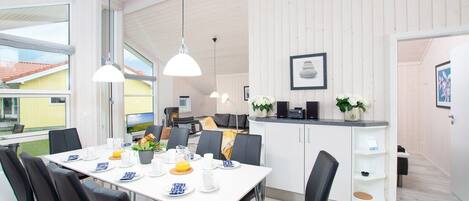 A modern dining area with a white table set for four, black chairs, and pendant lighting.