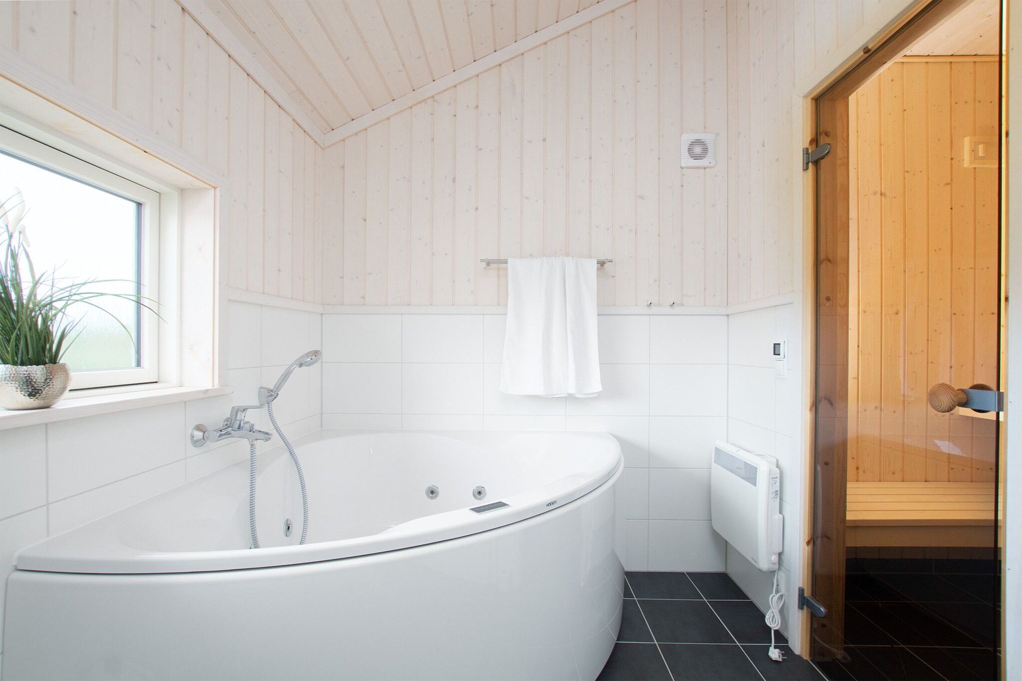 Un bagno moderno con una vasca freestanding, una finestra con una pianta e una porta in legno.