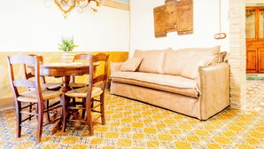 Una habitación con un sofá beige, sillas de madera, una mesa de comedor y baldosas de suelo estampadas.
