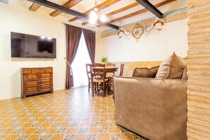 A living room with a sofa, a wooden cabinet, a dining table with chairs, and a TV mounted on the wall.