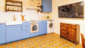 Cocina compacta con armarios azules, lavadora, microondas y un mueble de madera.
