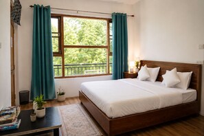 A bedroom with a wooden bed, white bedding, a nightstand with a lamp, a window with curtains, and a small table with books and plants.
