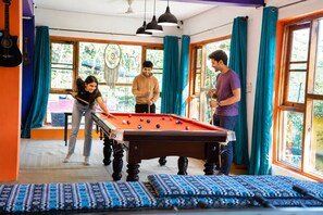 Una mesa de billar en una habitación con ventanas amplias y cortinas.