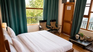 A bedroom with a bed, a chair, a small table with items, and a view of greenery outside. - Loopin Mcleodganj  (Dharamshala)