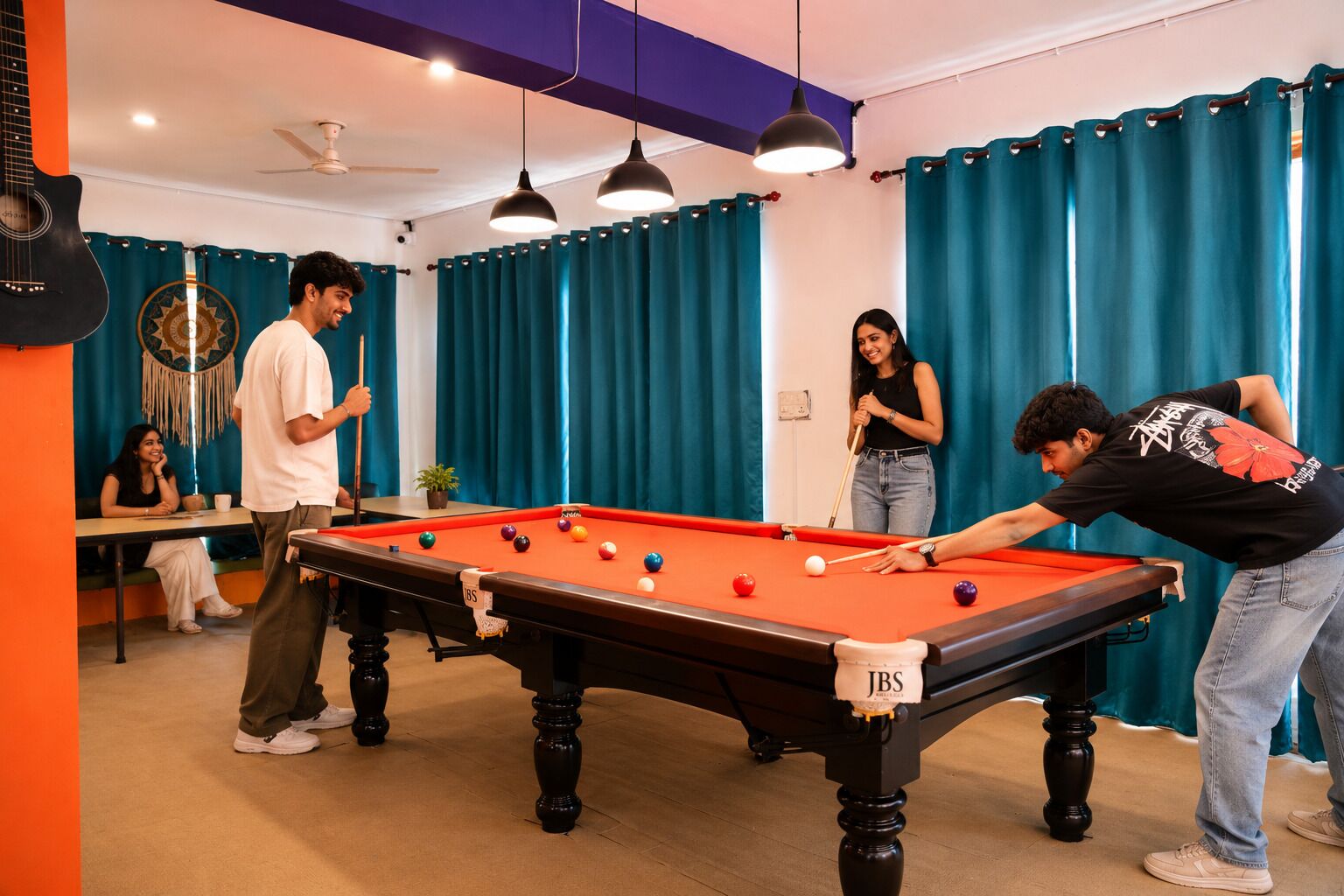 Une table de billard dans une pièce aux rideaux turquoise, dotée d’un ventilateur de plafond et de luminaires suspendus.