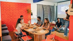 A group of people seated around a wooden table in a room with a brick wall and a projector screen displaying 'A FILM FESTIVAL.'