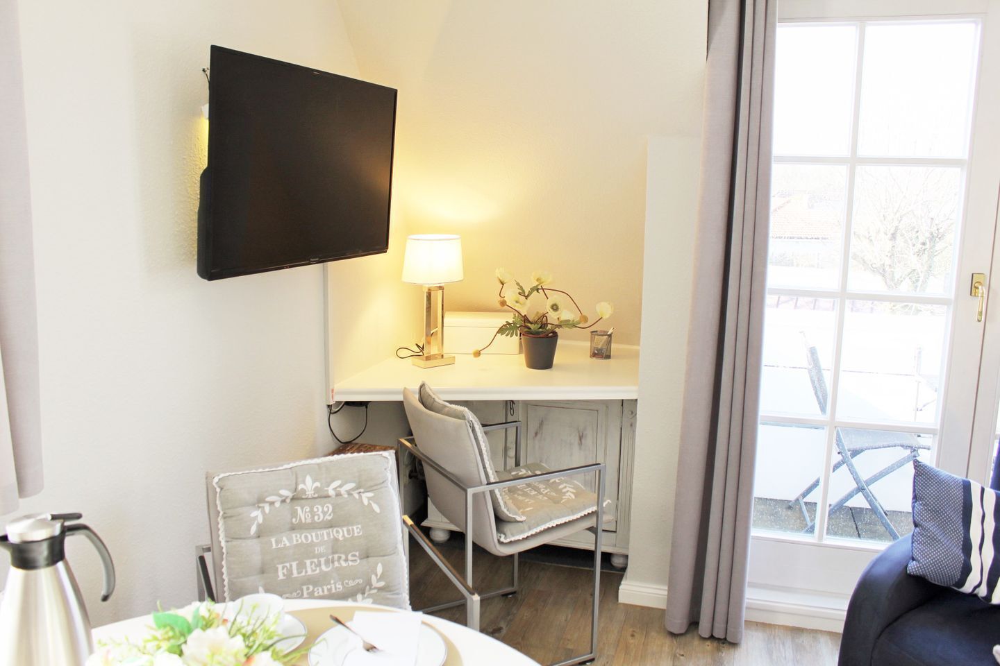 Een kamer met een wandgemonteerde flatscreen-tv, een tafel met een bordje, een stoel en uitzicht buiten door een raam.