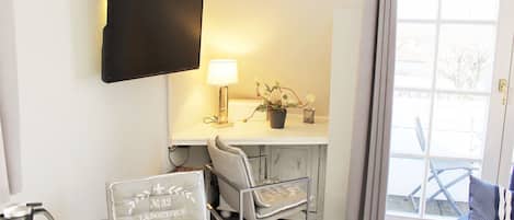 Een kamer met een wandgemonteerde flatscreen-tv, een tafel met een bordje, een stoel en uitzicht buiten door een raam.