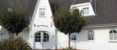 A traditional building with a pointed roof, a central entrance with a door, and the name 'Bitt Singst' on the facade.