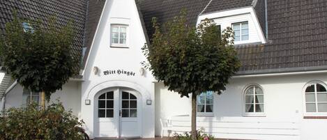 A traditional building with a pointed roof, a central entrance with a door, and the name 'Bitt Singst' on the facade.