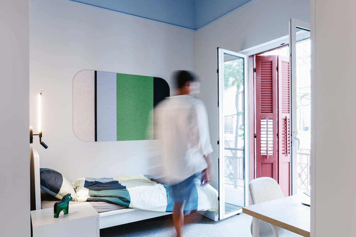 Una habitación con cama, escritorio, silla, lámpara colgante y puerta corredera de vidrio.