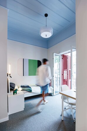 A room with a bed, a desk, a chair, a hanging light fixture, and a sliding glass door. - Makarta House (Limassol)
