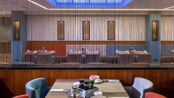 A restaurant with a modern interior, featuring a central dining area with tables and chairs, a decorative wall with vertical lines, and a skylight above.
