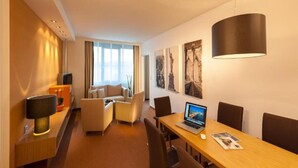 Habitación de hotel con una mesa de comedor, sillas, una computadora portátil, un televisor y obras de arte en las paredes.