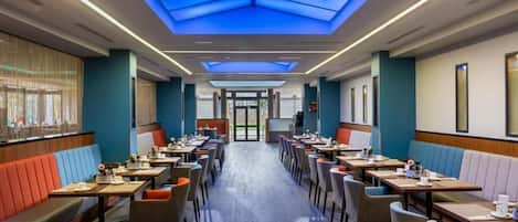 Un espace de restauration d’hôtel avec des banquettes et des tables, un plafond en verrière et une vue à travers les portes vitrées.