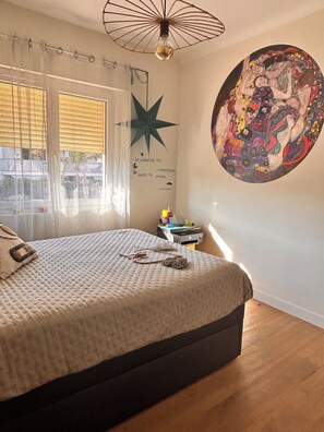 Ein Schlafzimmer mit einem Bett, einer Sterndekoration, einem Wandbild und einem Schreibtisch mit einem Drucker.