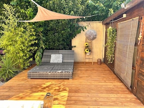 A wooden deck with a raised platform, surrounded by greenery and a wooden fence. - The Good Life… (Fréjus)